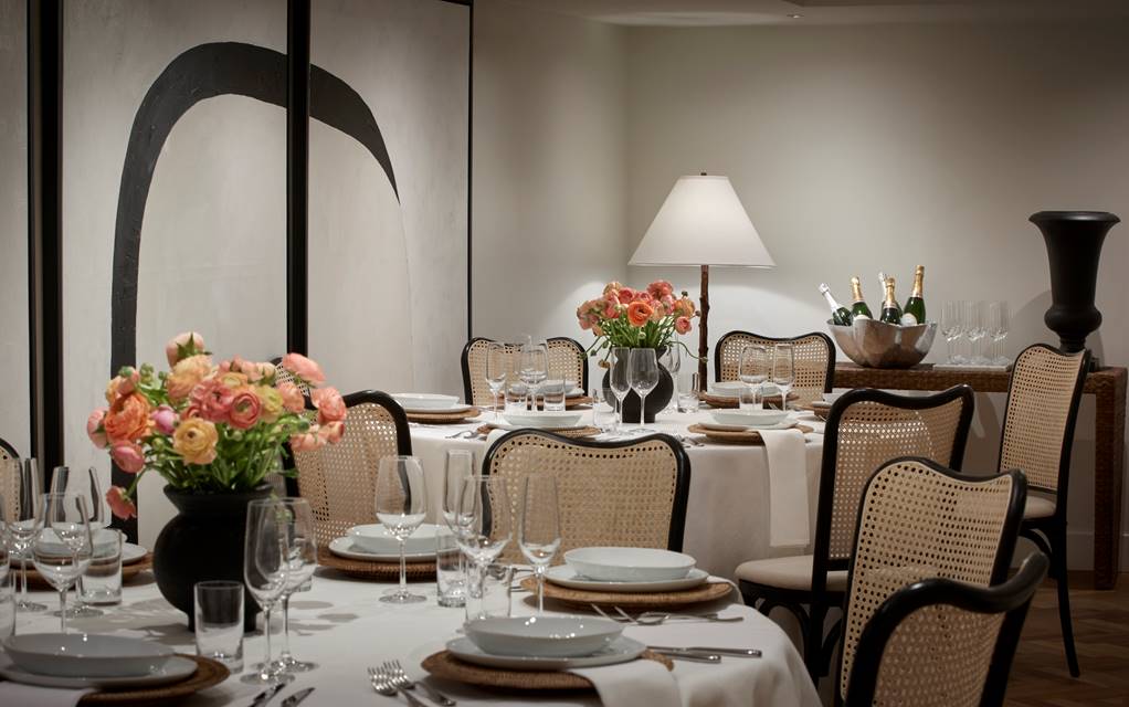 A private dining table set with floral arrangements, champagne bottles, and rattan-backed chairs at the Lyle DC hotel.