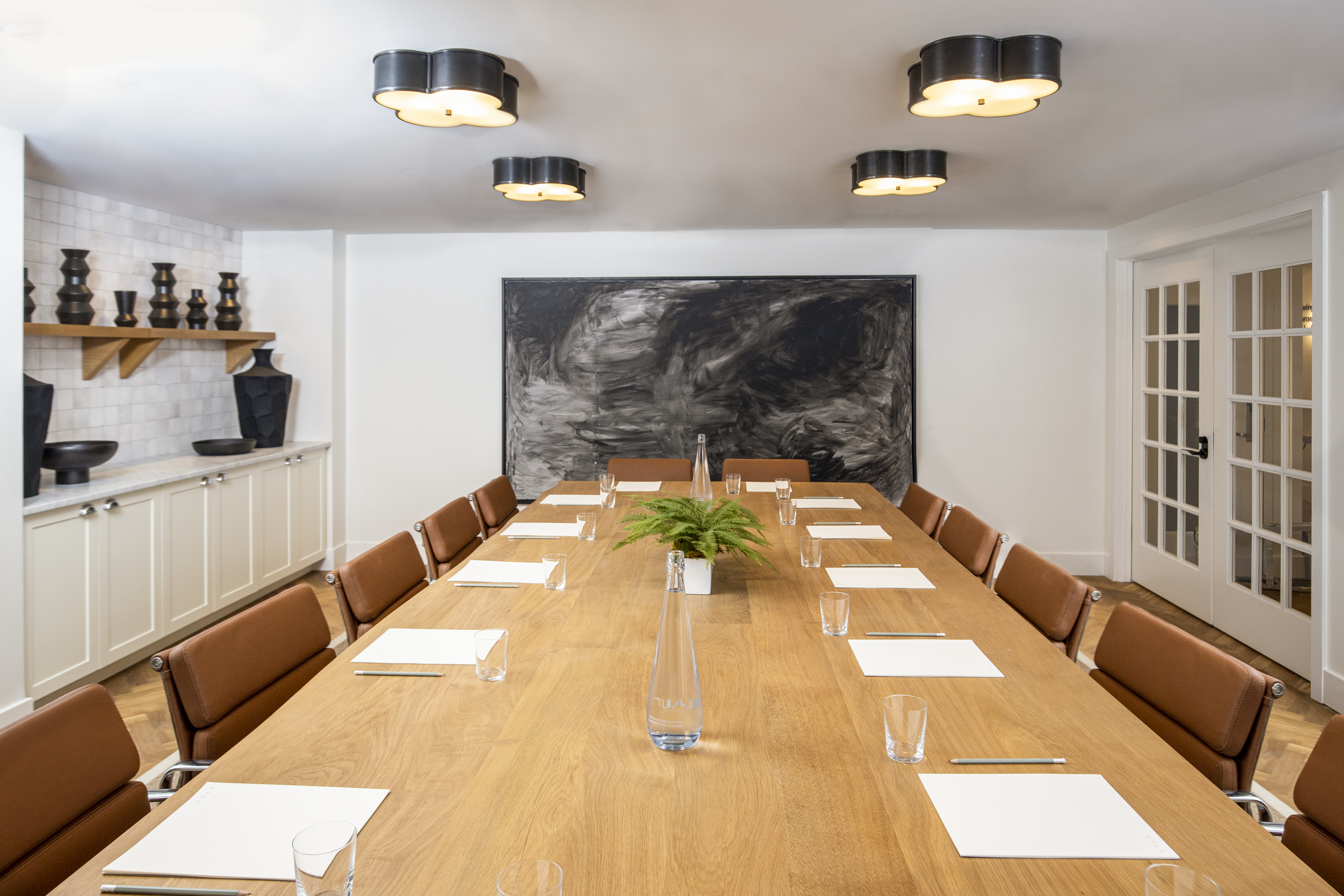 A modern meeting room at Lyle DC with a long wooden table, brown leather chairs, minimalist decor, and contemporary artwork.