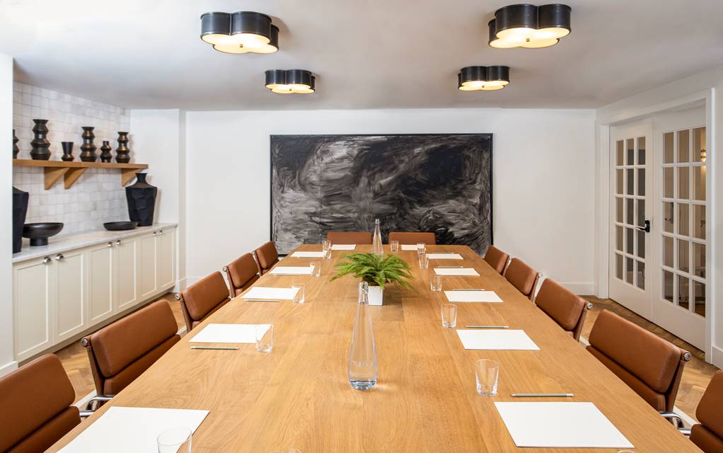 A modern meeting room at Lyle DC with a long wooden table, brown leather chairs, minimalist decor, and contemporary artwork.