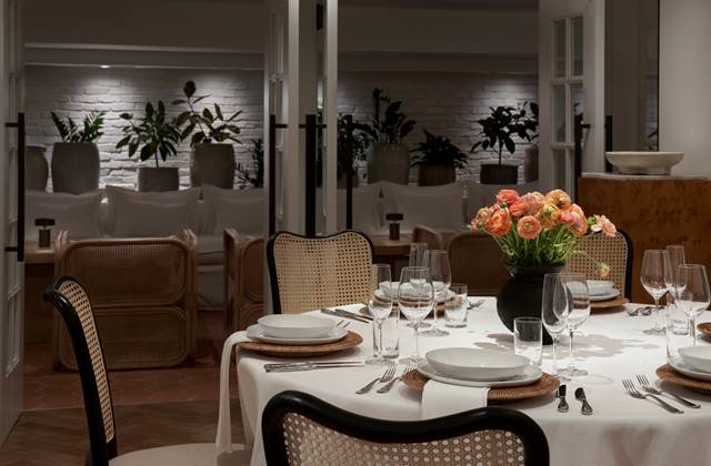 A dining room with a set table, wicker chairs, and flowers