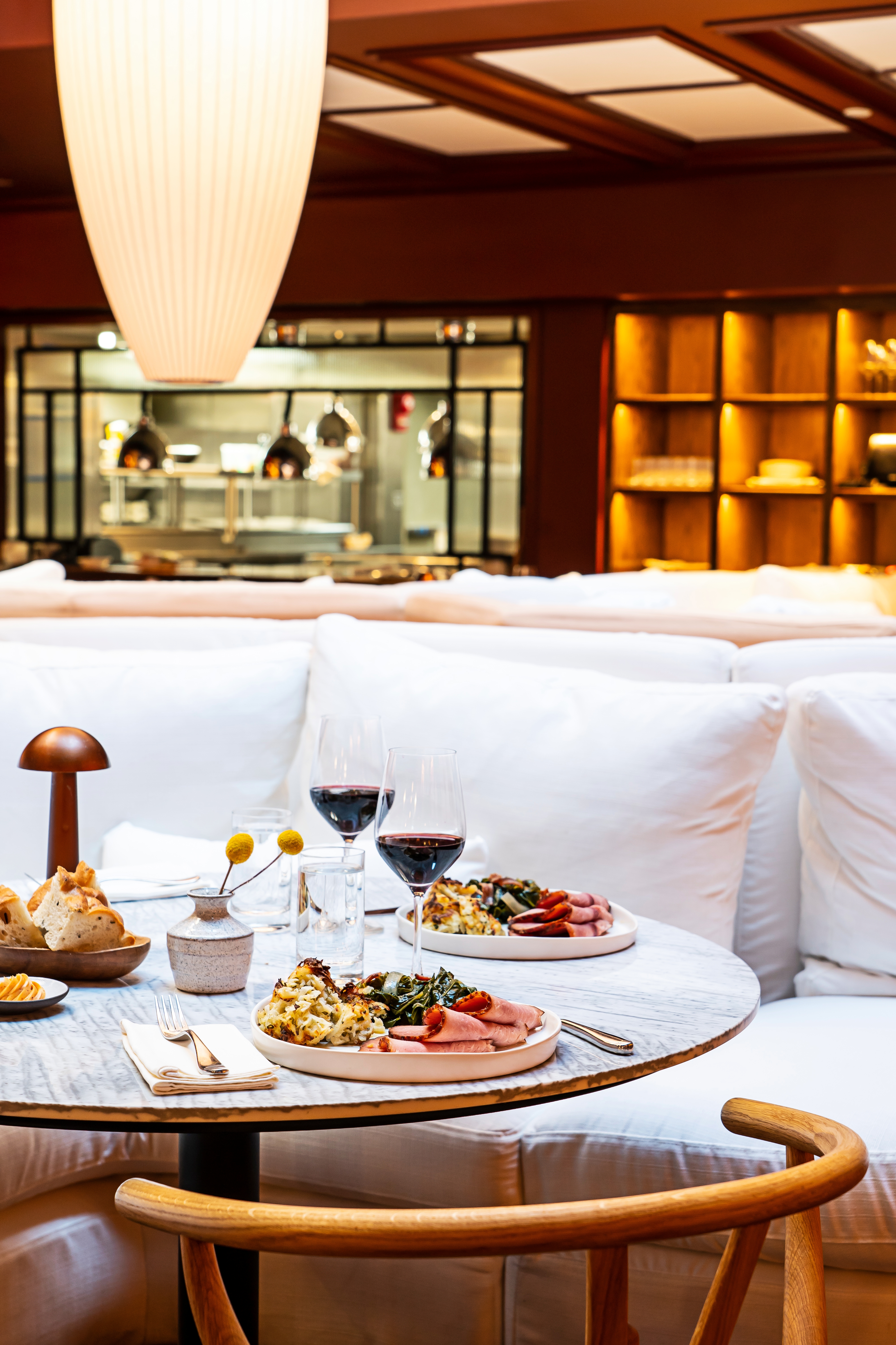A dining area with a table set for two, plates of food, and wine glasses in front of a white couch.