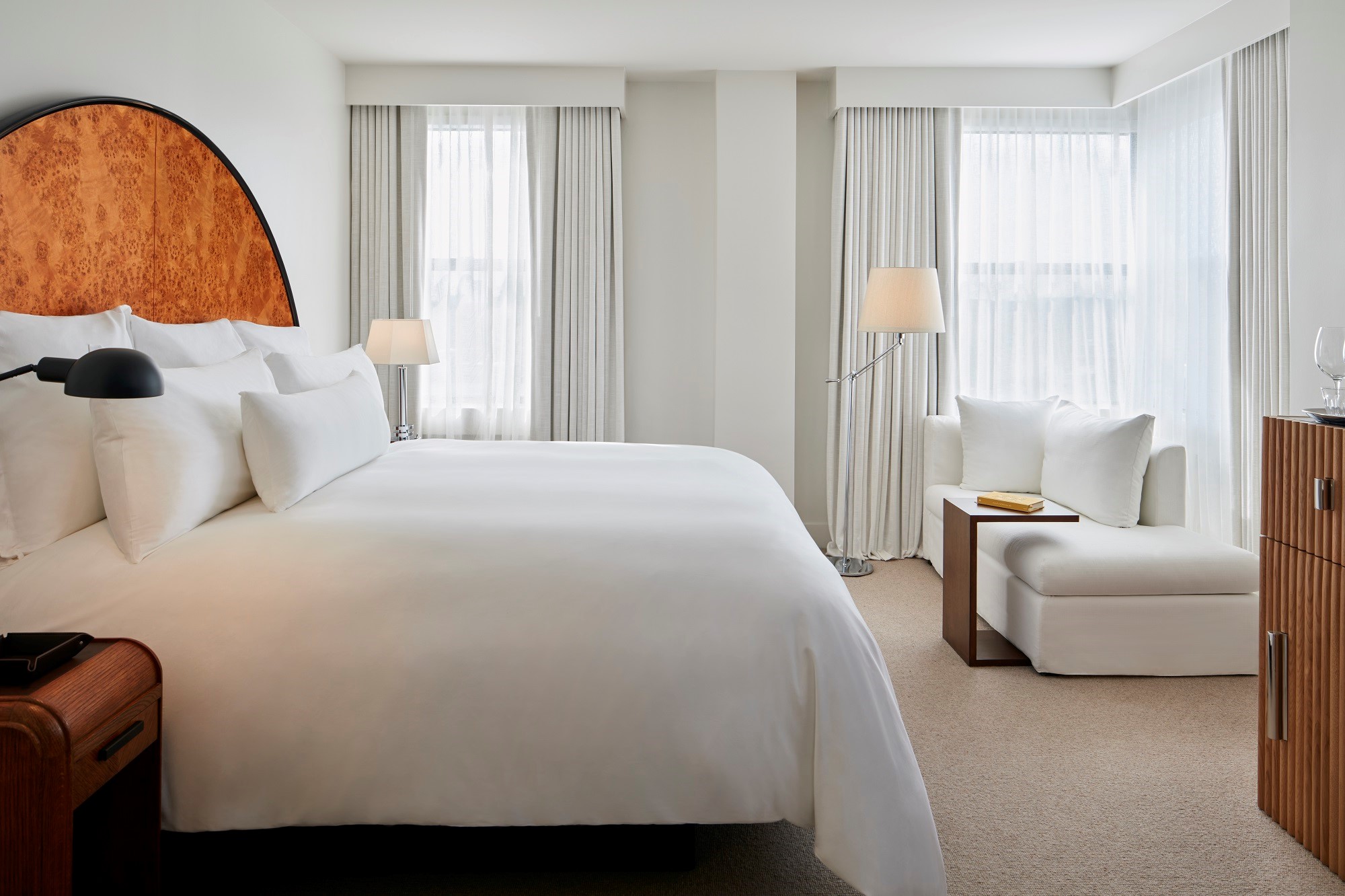 Bed with white sheets and Burl wood art deco headboard at a king hotel room at Lyle DC.