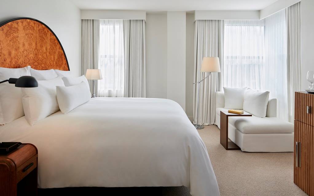 Bed with white sheets and Burl wood art deco headboard at a king hotel room at Lyle DC.