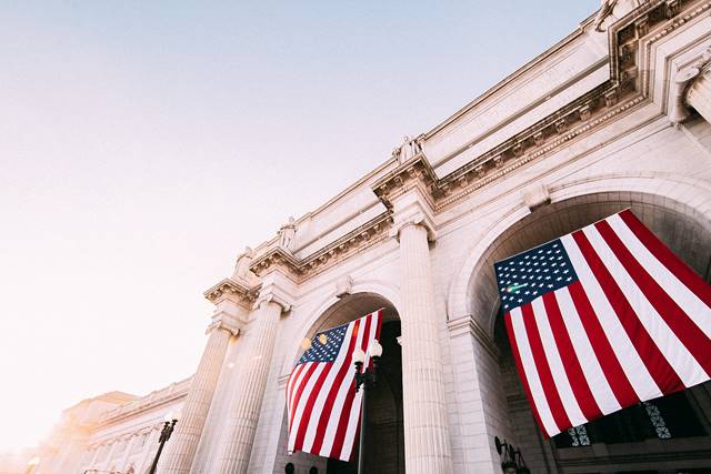 The grand entrance of Union Station in Washington, DC, with large American flags hanging from its classical columns.