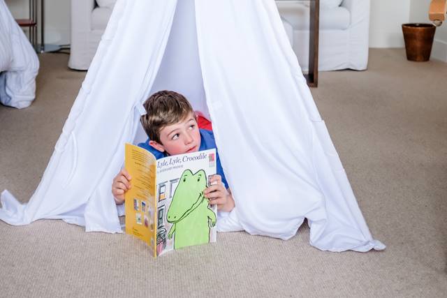 Child reading 'Lyle Lyle Crocodile' in teepee in Lyle guest room.