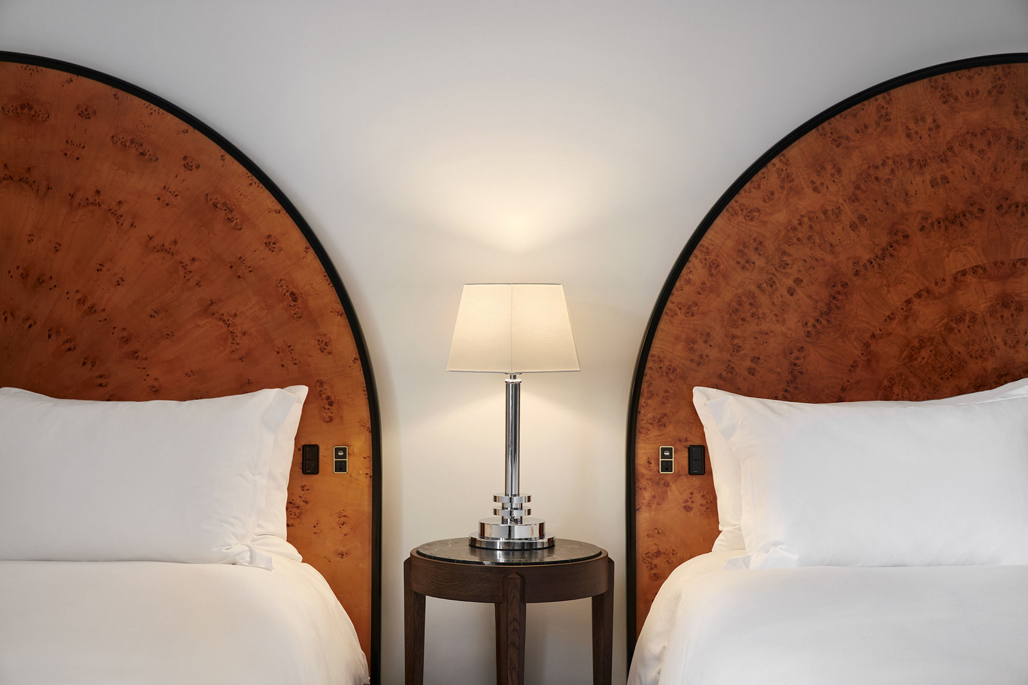 Two twin beds with curved wooden headboards and crisp white linens flank a central lamp in a Lyle Washington DC hotel room.