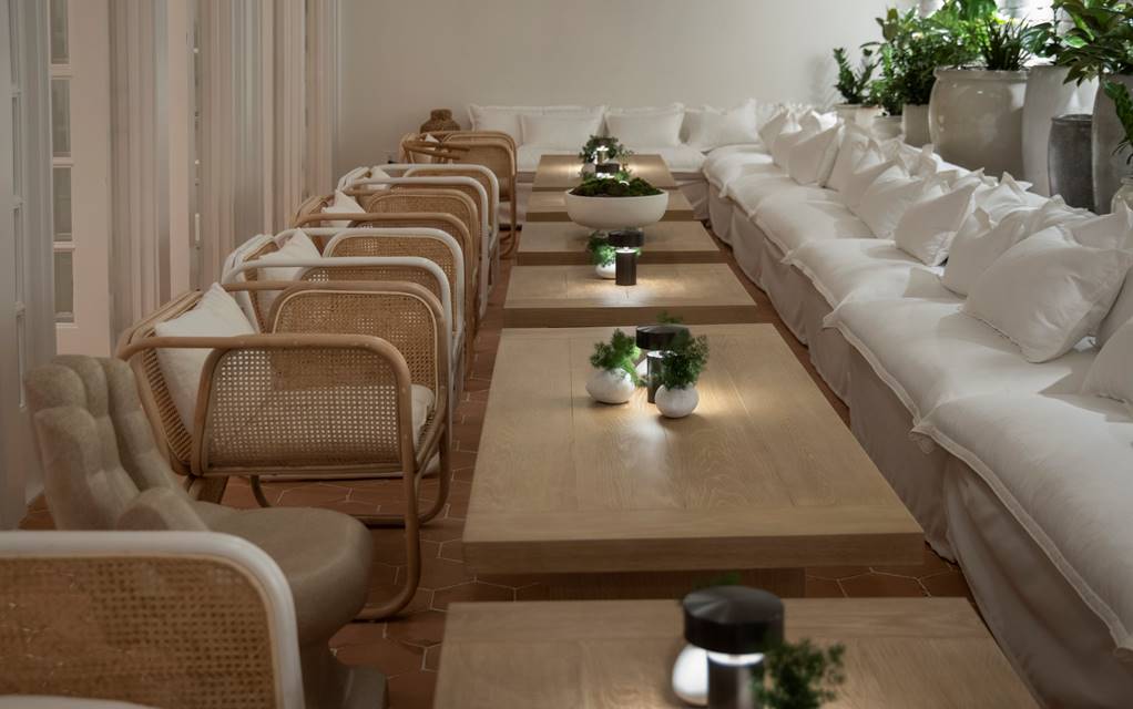 Looking down the long tables in the Conservatory with wooden tables and white seating at Lyle DC.