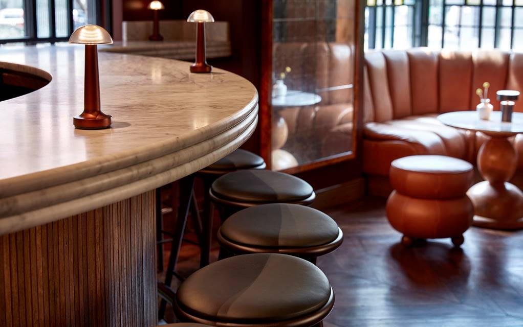A sleek bar at Lyle's Bar with a curved marble countertop, leather barstools, and warm ambient lighting.