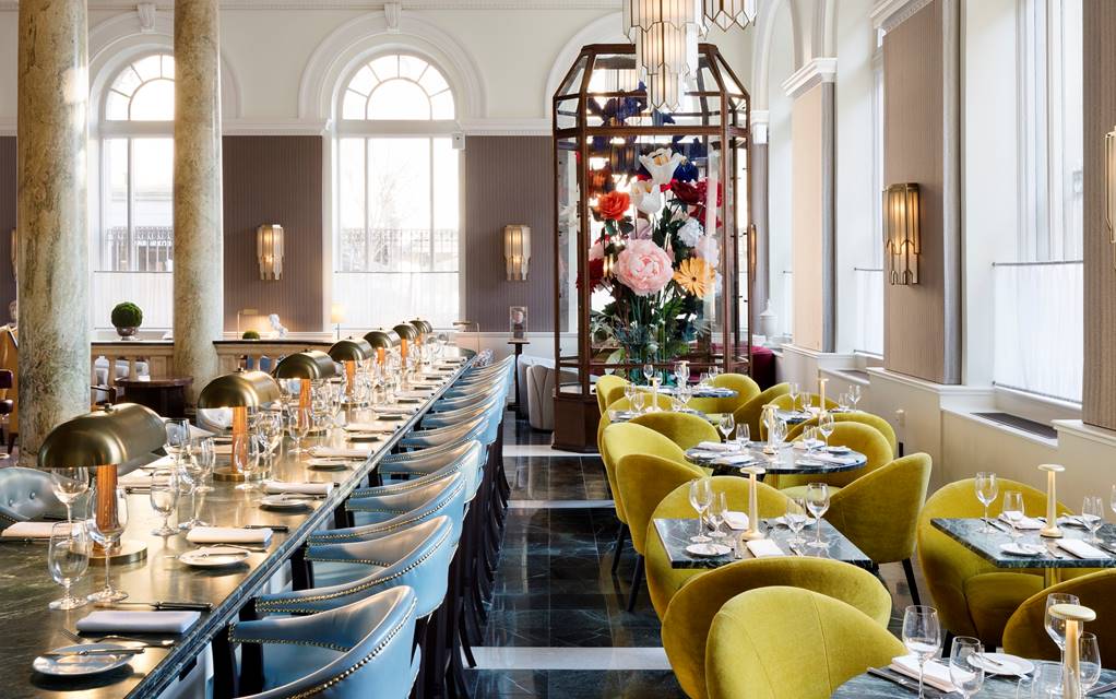 The stylish interior of Cafe Riggs in DC with elegant green chairs, gold accents, and a center piece of oversized flowers.