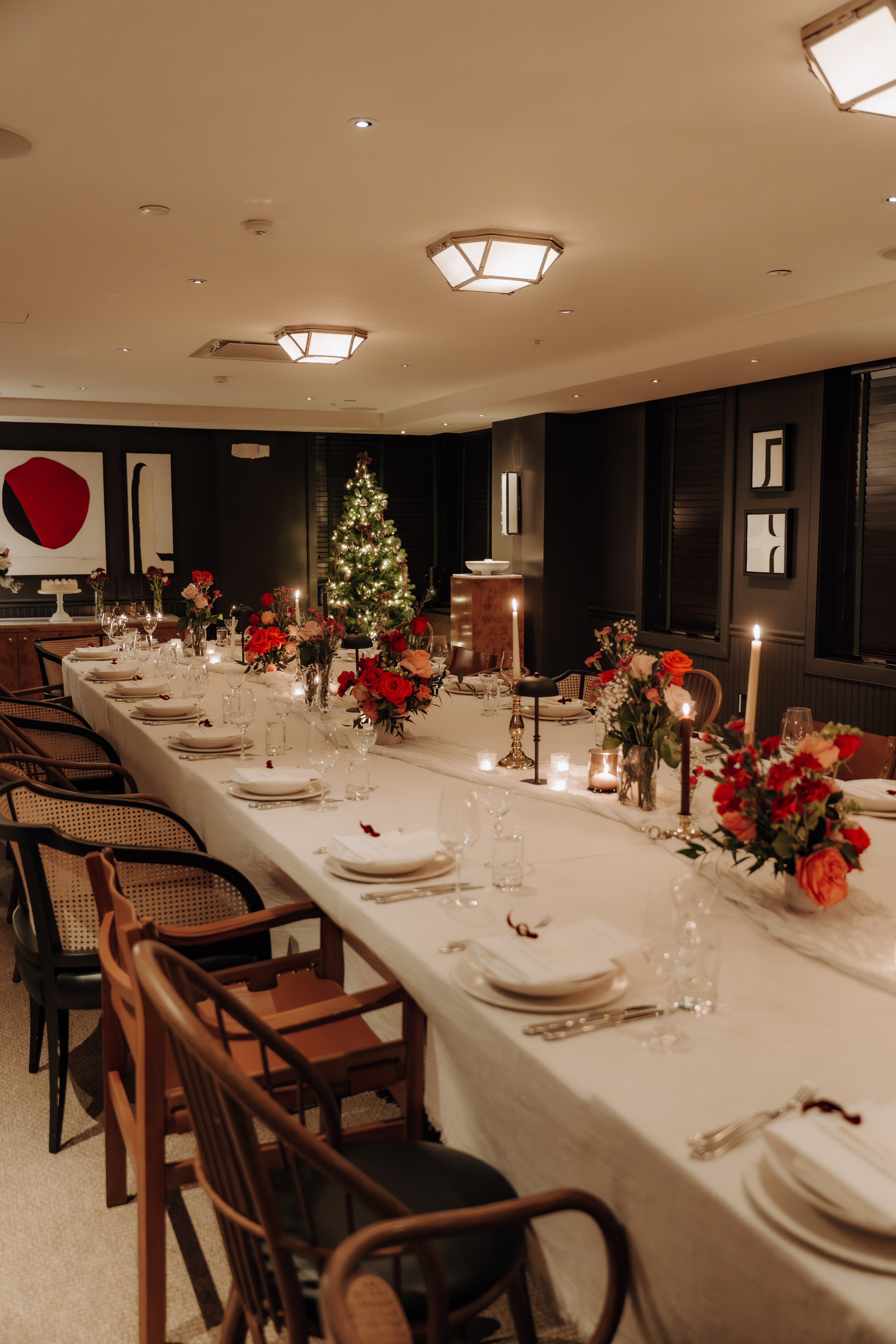 A long table set for dinner with a white tablecloth, flowers, candles, and a Christmas tree in the background.