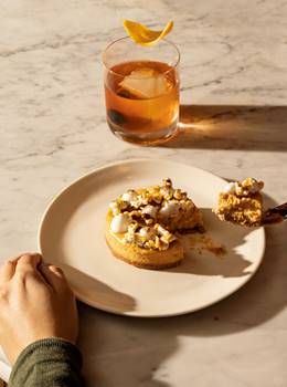 Autumnal dessert being lifted on fork with cocktail in background