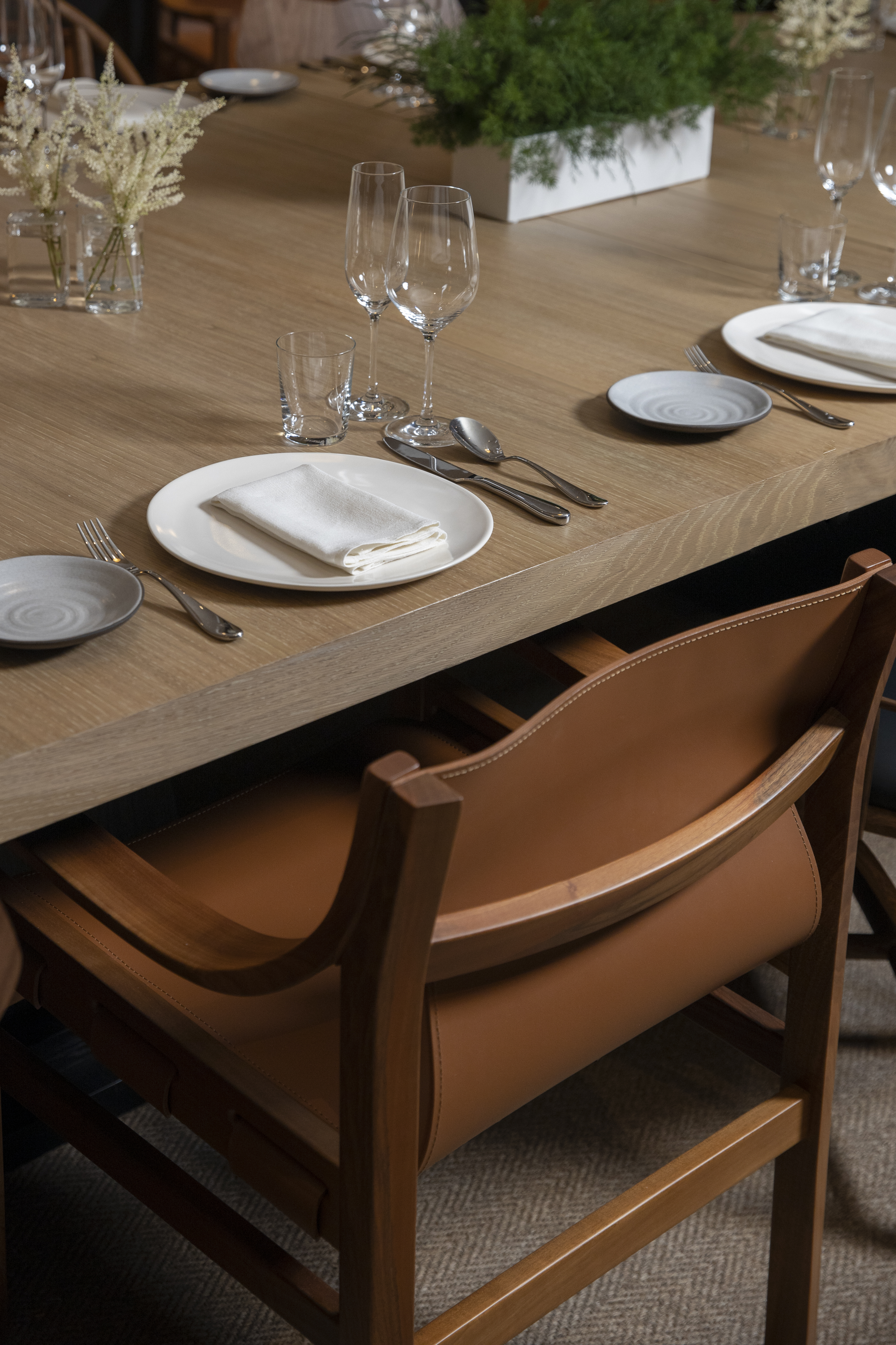 A dining table set with plates, glasses, and utensils, with leather chairs tucked in.