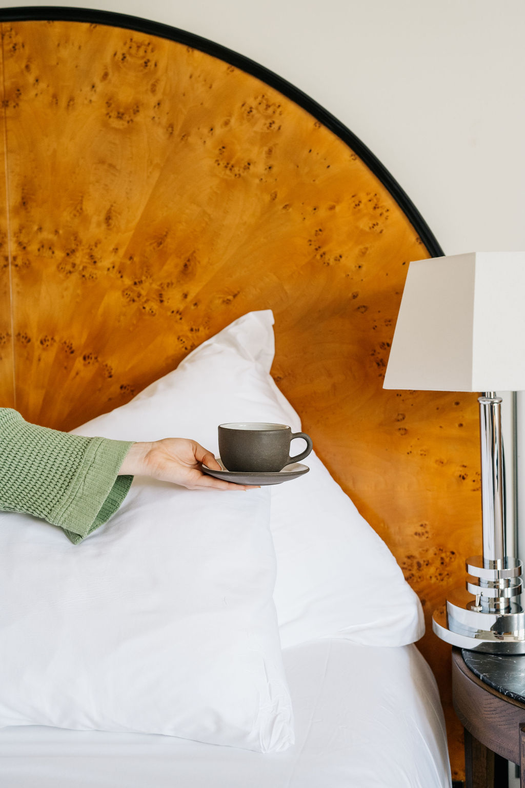 Hand holding a mug in front of burl wood headboard