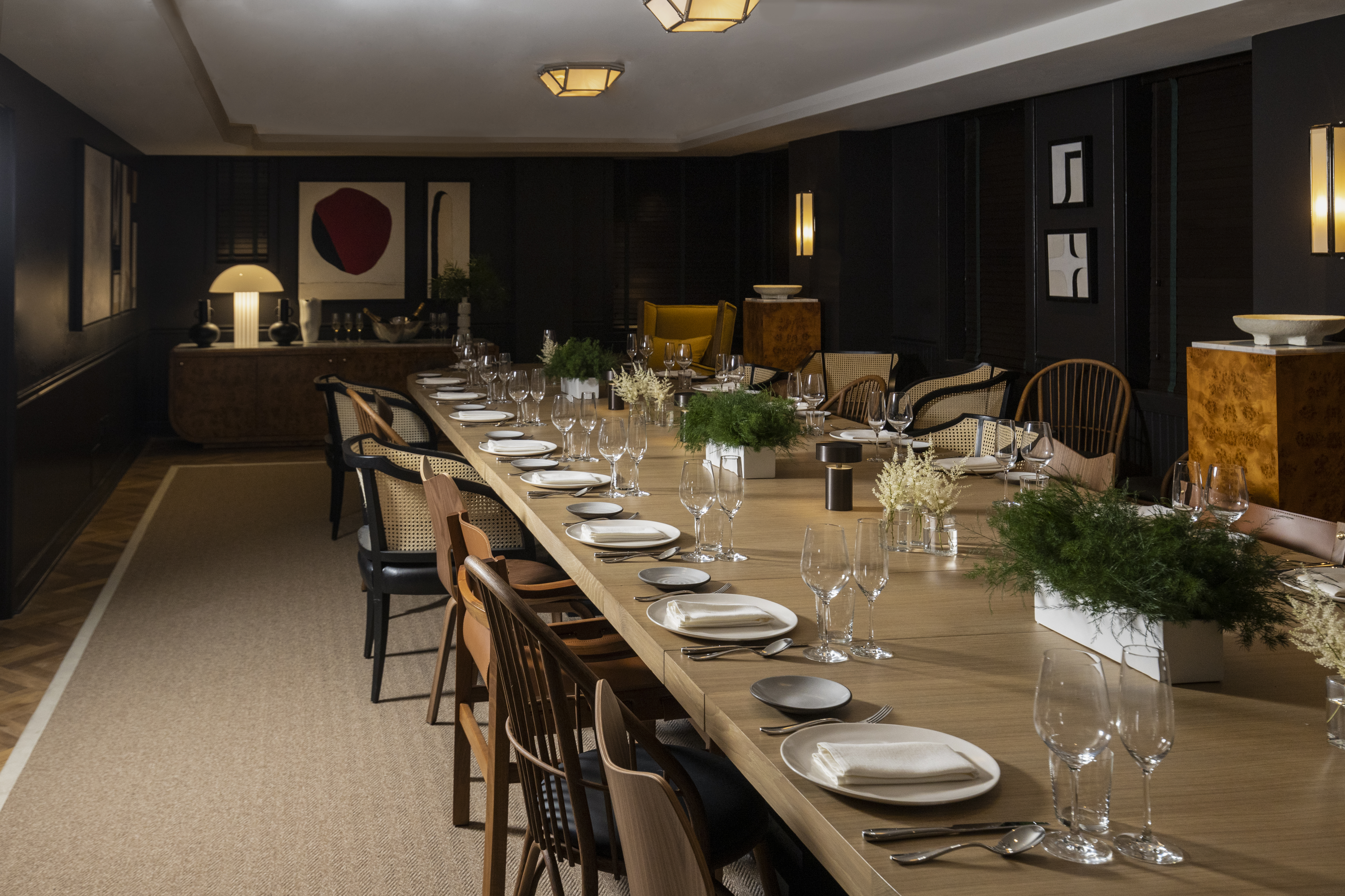 A long dining table set with plates, glasses, and greenery in a meeting room.
