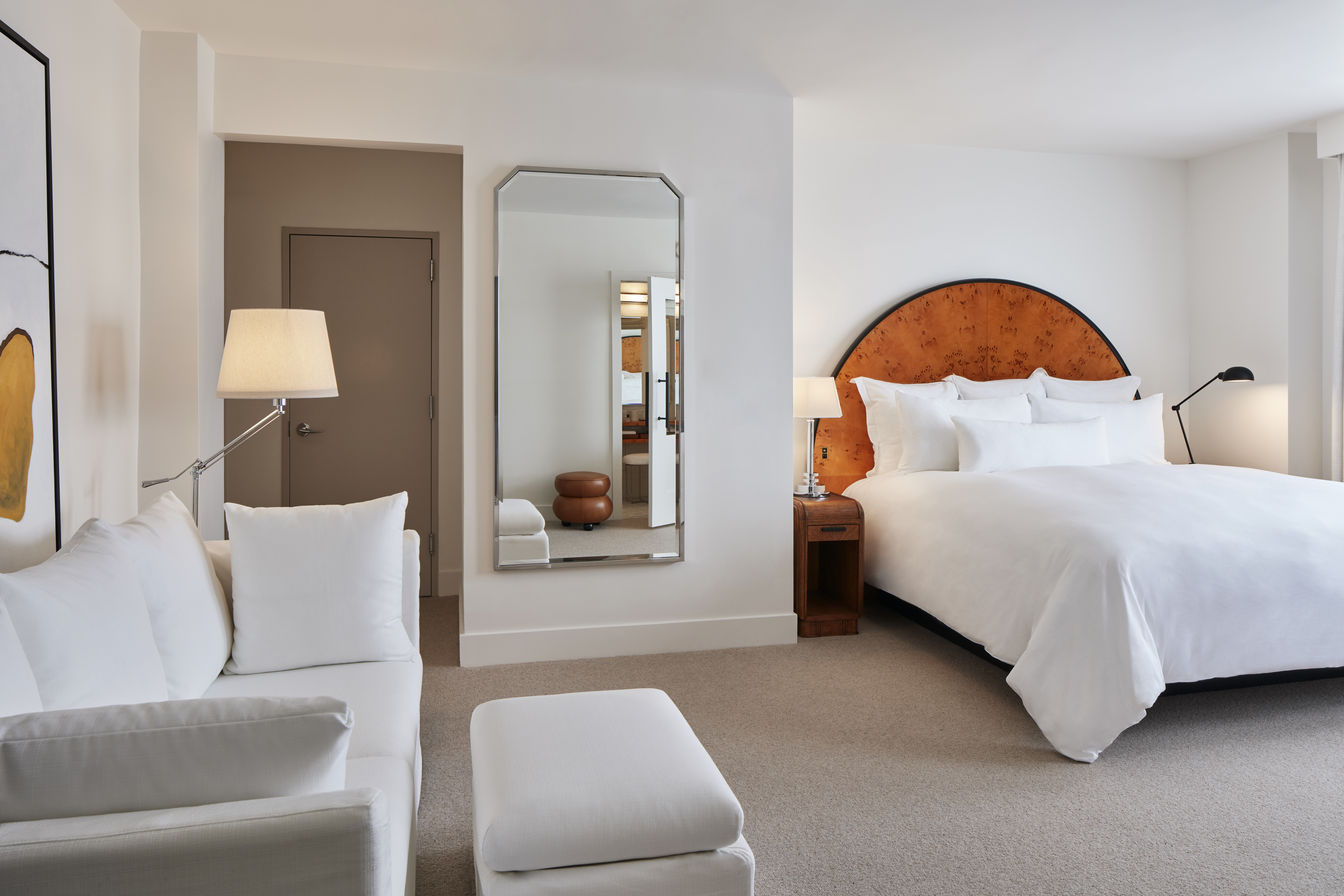 A wide view of a hotel room with a large bed, a sofa, and a mirror