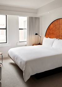 A modern hotel room at Lyle Washington DC, featuring a king-sized bed, arched wooden headboard, and minimalist decor.